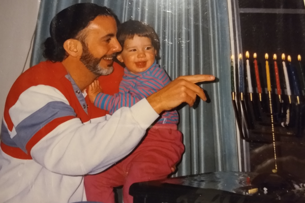 Cynthia Friedman being held by her father as toddler smiling in front of their menorah