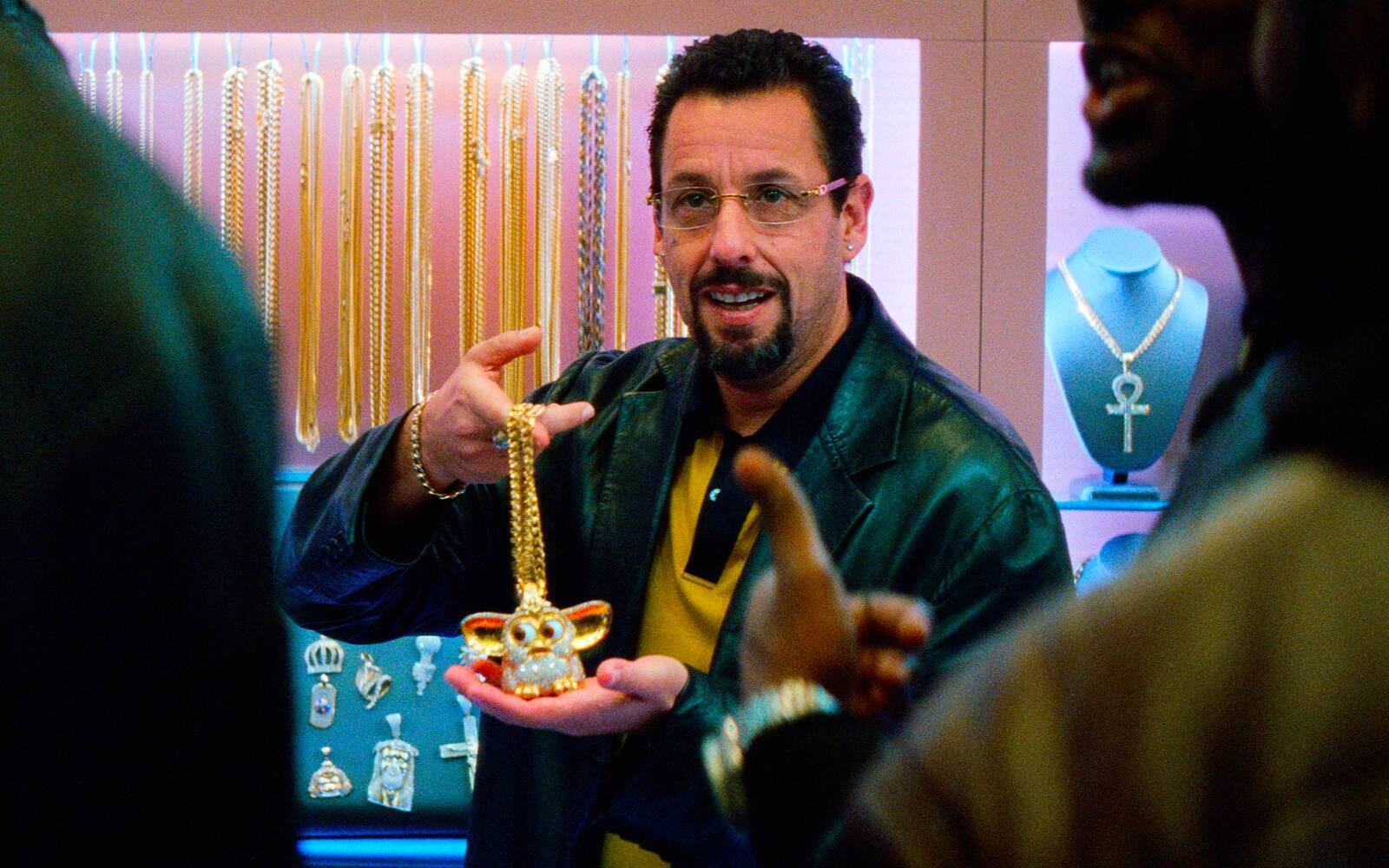 A man holding up a gold chain with a diamond encrusted Furby on it.
